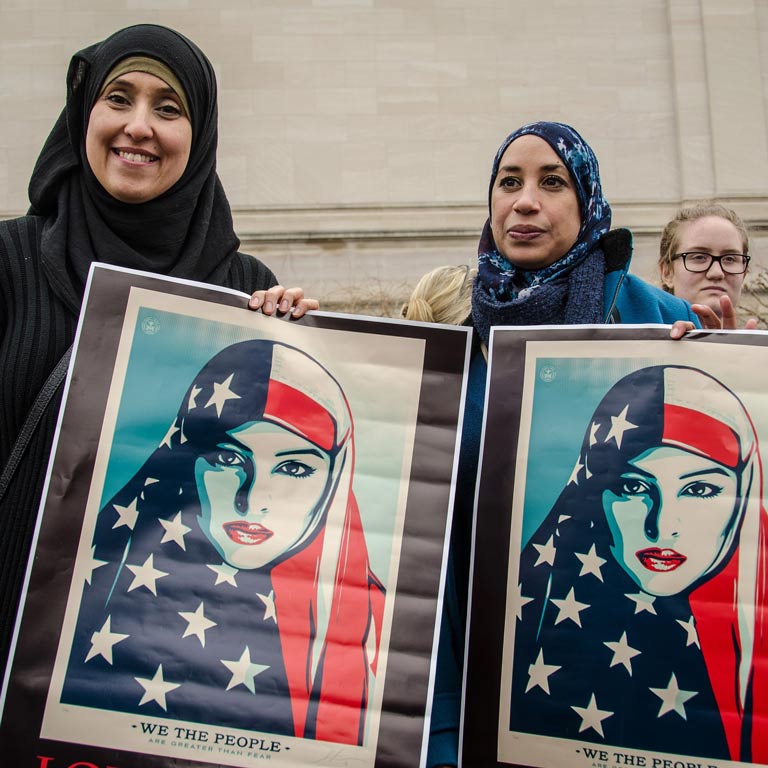 Two muslim women holding up art of Muslim women wearing an American flag over their heads