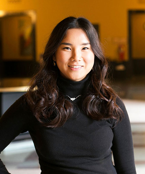 Faculty member Chinbo Chong poses in a black sweater against a gold and black background.