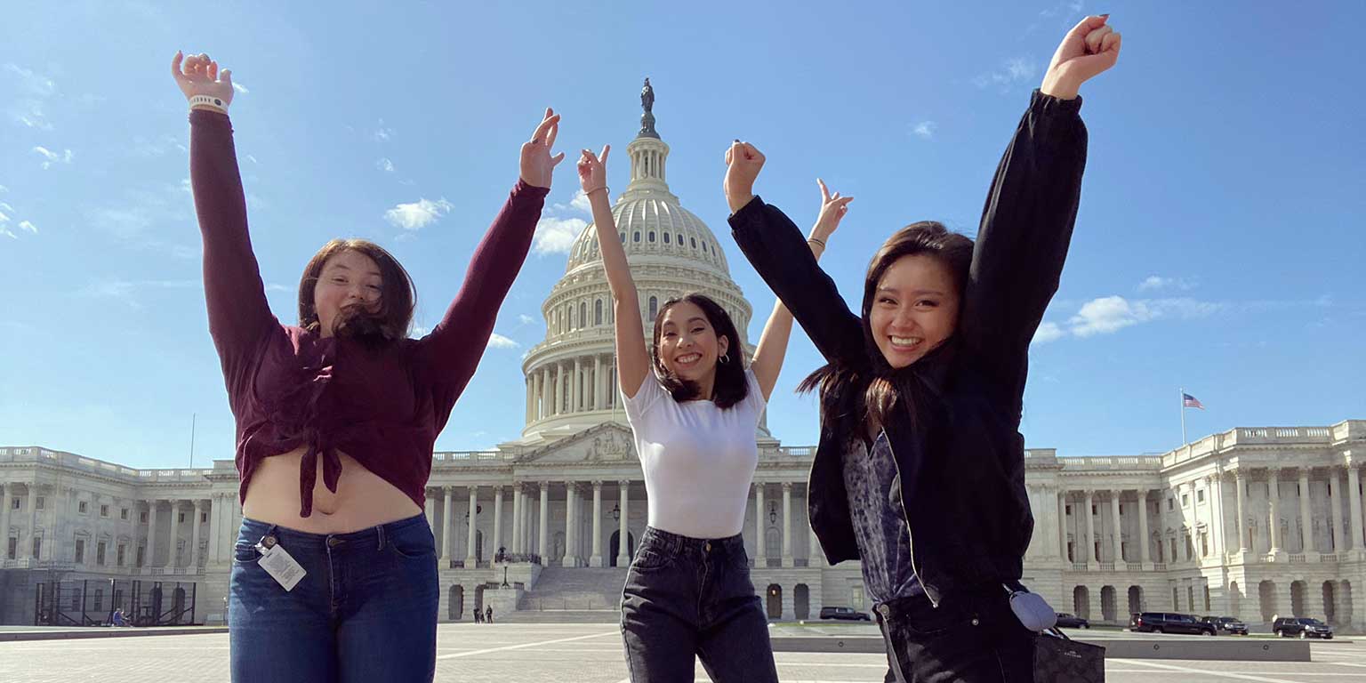 Three Political Science students pose in front of the Capitol Building, jumping in the air.