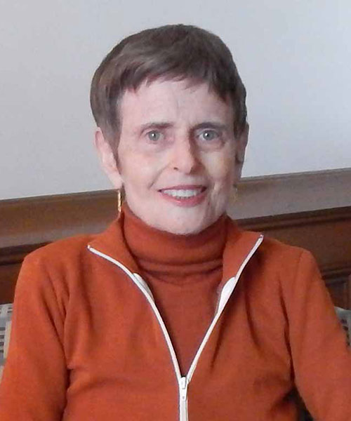 Faculty member Dina Spechler poses in a red sweater against a gray background.