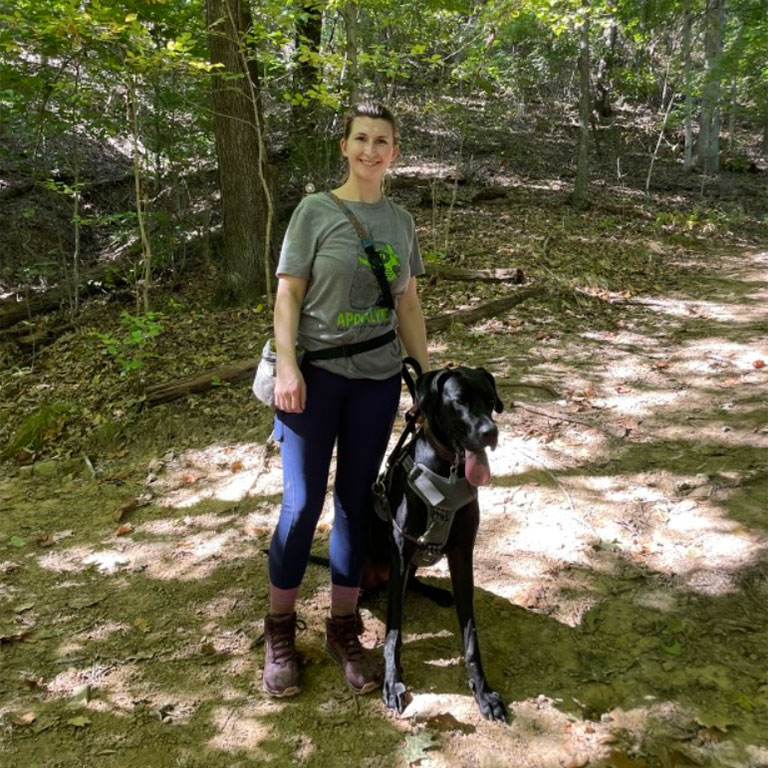 Anna Adams poses on a hiking trail alongside a large black dog.