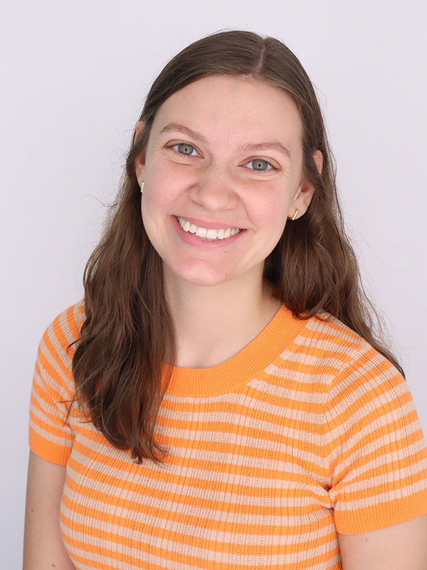 A headshot of Mary Adams, who wears an orange sweater.