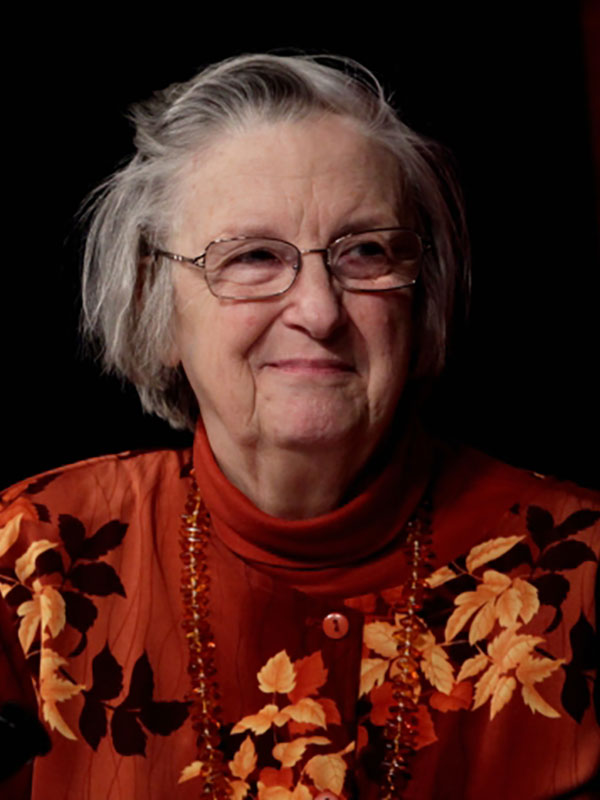 A headshot of Lin Ostrom, who wears a red sweater and poses against a black background.