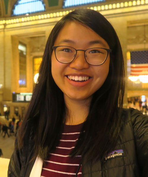 Undergraduate student Nancy Ni poses against a bright yellow background.