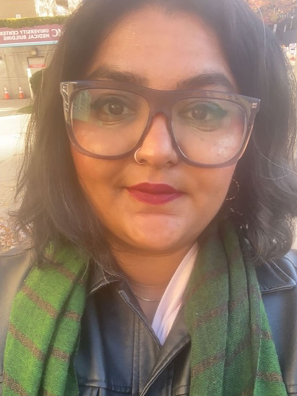 A headshot of Aashna Khanna, who wears glasses and a green scarf.
