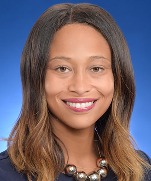 Alumna Tiffany Benjamin poses in a navy blue suit against a blue background.